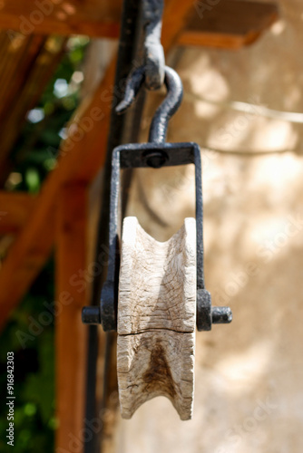 Close-up of an old black iron and weathered wood pulley from a well, shot from a low angle on the porch of a rural house in Spain.