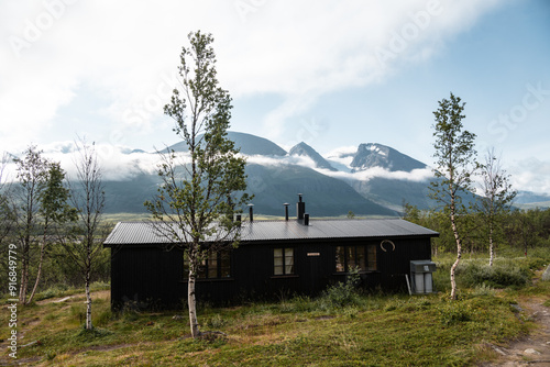 Akkastugorna, Swedish Lapland, Sweden - Cabin for Hikers on Padjelantaleden in National Park Stora Sjöfallet. Blue sky and Mount Akka in mystical clouds. birch tree forest in front. photo