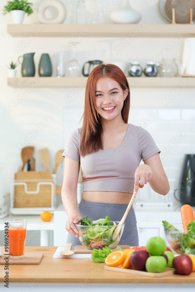 A young woman in athletic wear smiles brightly while preparing a fresh salad in a stylish, modern kitchen. A young woman in athletic wear smiles brightly while preparing a fresh salad in a stylish, modern kitchen.