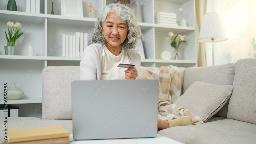 Smiling mature woman with grey hair holding a credit card and using laptop, enjoying online shopping or managing her finances. Smiling mature woman with grey hair holding a credit card and using laptop, enjoying online shopping or managing her finances.