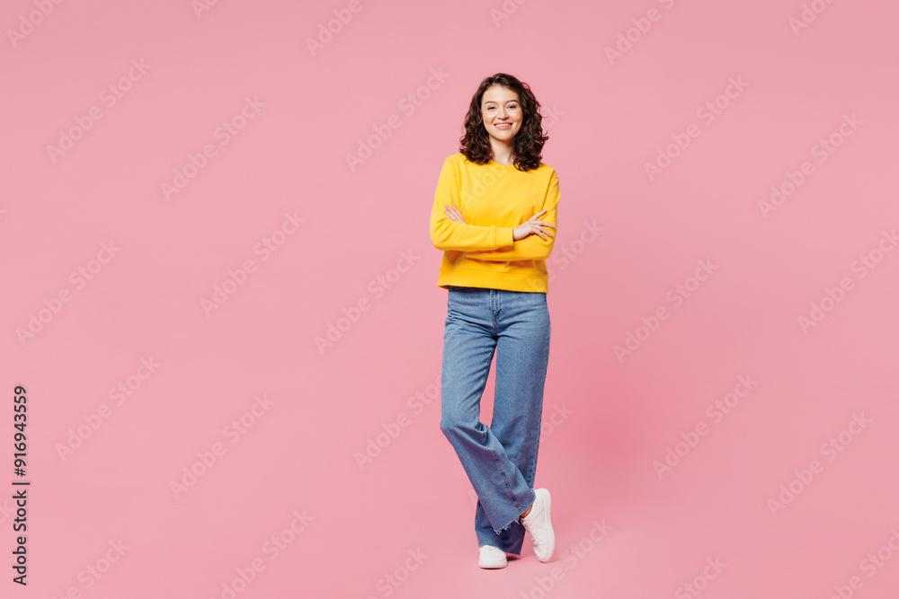 Full body smiling happy young woman wearing yellow sweatshirt casual clothes hold hands crossed folded looking camera isolated on plain pastel light pink background studio portrait. Lifestyle concept.