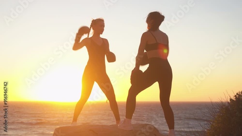 Wallpaper Mural Sporty backlit female fighters practicing boxing on rock overlooking seascape and sky at beach during bright sunset. Determined young women boxers are giving high-five as they celebrate in nature.  Torontodigital.ca