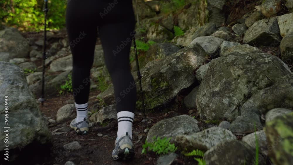 Back view of woman hiking in mountains with trekking poles in summer. She wears trekking shoes and a backpack. Walking through dense forest and rocky trail. Outdoor adventure in nature. Slow motion. Back view of woman hiking in mountains with trekking poles in summer. She wears trekking shoes and a backpack. Walking through dense forest and rocky trail. Outdoor adventure in nature. Slow motion.
