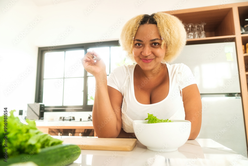 Happy young African American curvy woman in kitchen eating green salad from bowl and smiling. Healthy lifestyle and diet concept. Plus size woman, body positivity. Happy young African American curvy woman in kitchen eating green salad from bowl and smiling. Healthy lifestyle and diet concept. Plus size woman, body positivity.