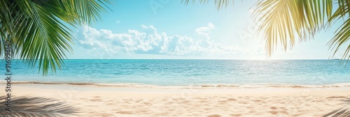 A serene beach scene with golden sand and clear blue sea under a sunny sky, featuring a palm leaf in the foreground and a tranquil ocean in the background photo