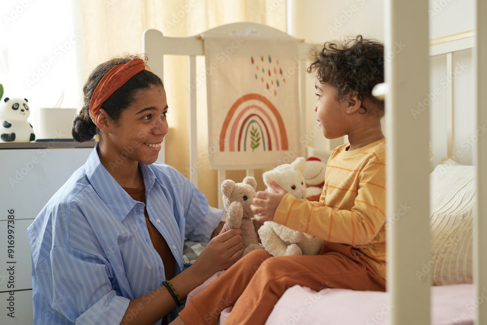 Obraz premium Smiling mother giving teddy bear to her delighted young son in cozy child bedroom. Interacting with toys, creating an atmosphere of warmth and joy