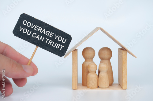 Hand holding signage with Coverage You Can Trust text with wooden family figure and mini house background photo