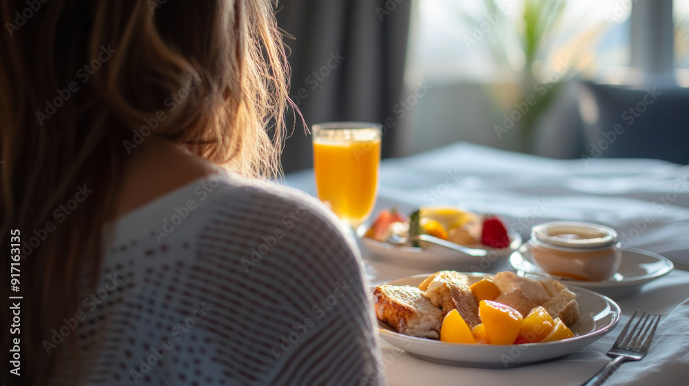 A woman enjoys breakfast in her hotel room, which was prepared by room service. A woman enjoys breakfast in her hotel room, which was prepared by room service.