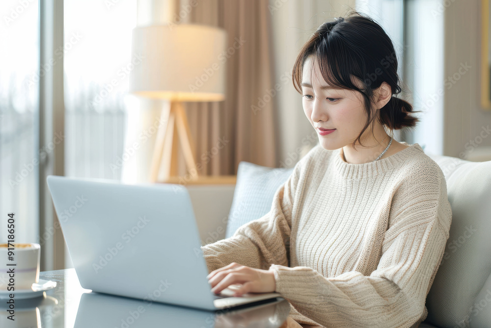A asian woman working on a laptop in a cozy indoor setting, exuding focus and productivity.
