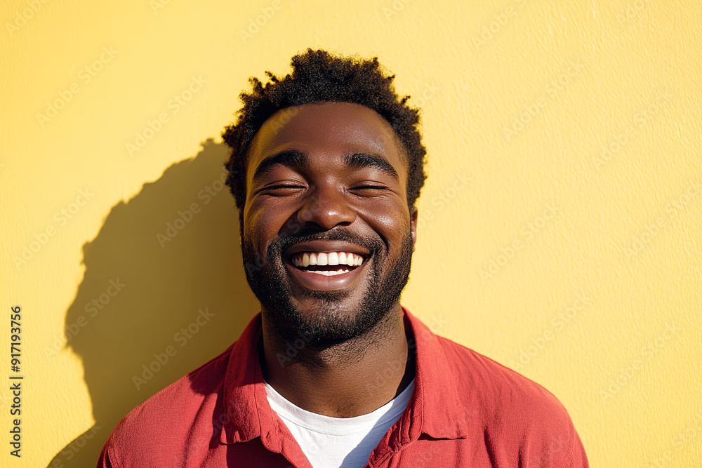 Professional Close-Up of a Black Man Smiling and Laughing in Red Shirt and White T-Shirt, Sunlight Enhancing His Joyful Expression Against Yellow Wall Professional Close-Up of a Black Man Smiling and Laughing in Red Shirt and White T-Shirt, Sunlight Enhancing His Joyful Expression Against Yellow Wall