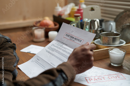 Person holding eviction notice at wooden table with various condiments and utensils scattered around showing urgent and distressing situation photo