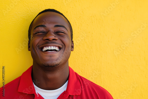 Smiling Black Man in Red Shirt with White T-Shirt Underneath, Laughing Joyfully on a Sunny Day with Sunlight Illuminating His Face, Against a Yellow Wall Background. High-Resolution Headshot Portrait 