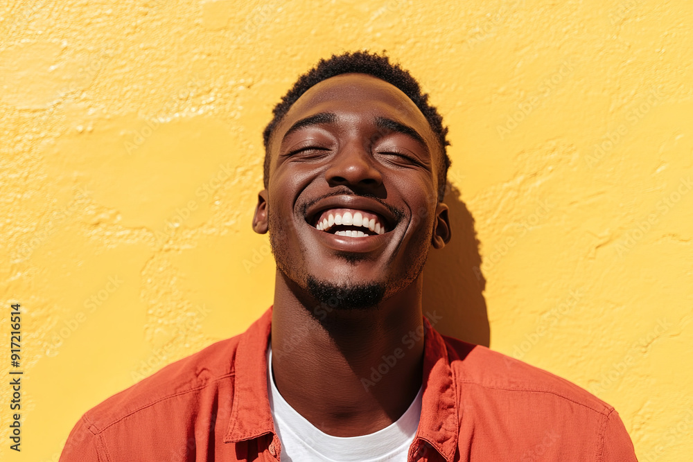 Smiling Black Man in Red Shirt with White T-Shirt Underneath, Laughing Joyfully on a Sunny Day with Sunlight Illuminating His Face, Against a Yellow Wall Background. High-Resolution Headshot Portrait 