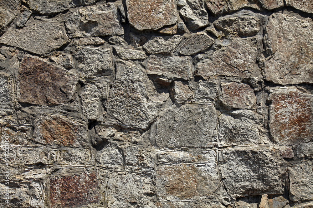 Granite wall, background. Surface of stone structure built of granite rocks (bricks). The wall texture of volcanic grey color. Fence with large gray stones on cement base in the rays of the sun Granite wall, background. Surface of stone structure built of granite rocks (bricks). The wall texture of volcanic grey color. Fence with large gray stones on cement base in the rays of the sun