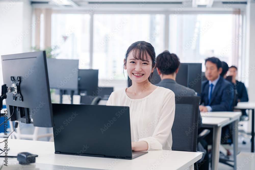 オフィスで笑顔でデスクワークをする若い女性 オフィスで笑顔でデスクワークをする若い女性