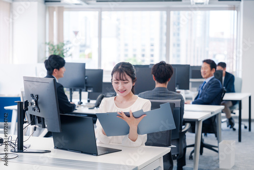 オフィスで笑顔でデスクワークをする若い女性