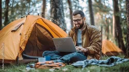 A man is sitting in a tent with a laptop, smiling