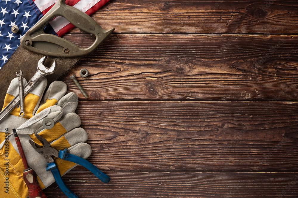 Labor Day in USA concept featuring an assortment of tools, gloves, and American flag on a wooden background Labor Day in USA concept featuring an assortment of tools, gloves, and American flag on a wooden background
