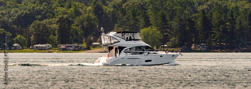 Panorama of a yacht cruising in the St. Lawrence River with an RV camprground in the background.