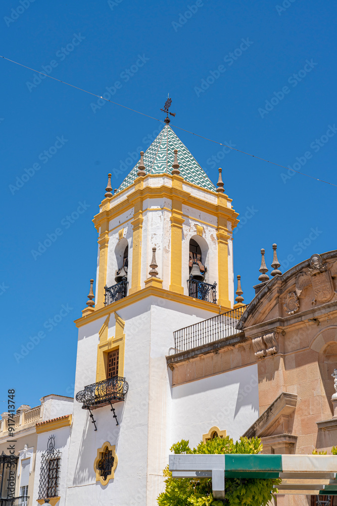 Fototapeta premium The stunning facade of the Church of Nuestra Señora de la Merced in Ronda, Spain, featuring twin bell towers and a central fountain under a bright blue sky. Perfect for themes of Spanish architecture