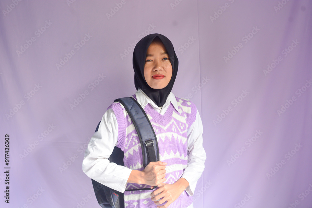 Portrait of a muslim schoolgirl carrying books in her hands and wearing a black backpack on an isolated background Portrait of a muslim schoolgirl carrying books in her hands and wearing a black backpack on an isolated background