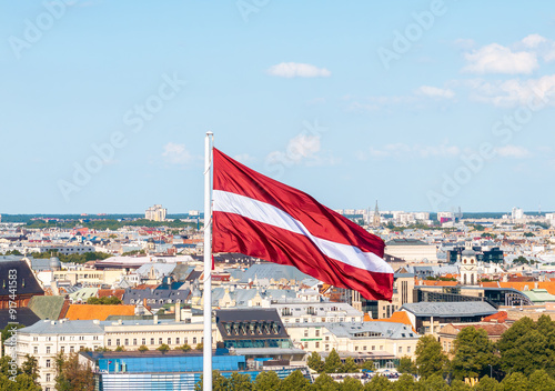 Latvian national flag waving with Riga cityscape in the background photo