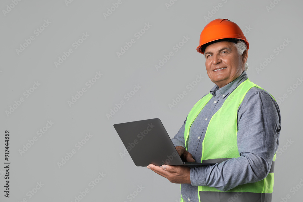 Engineer in hard hat with laptop on grey background, space for text Engineer in hard hat with laptop on grey background, space for text