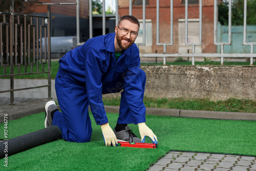 Happy young man in uniform installing artificial turf outdoors photo