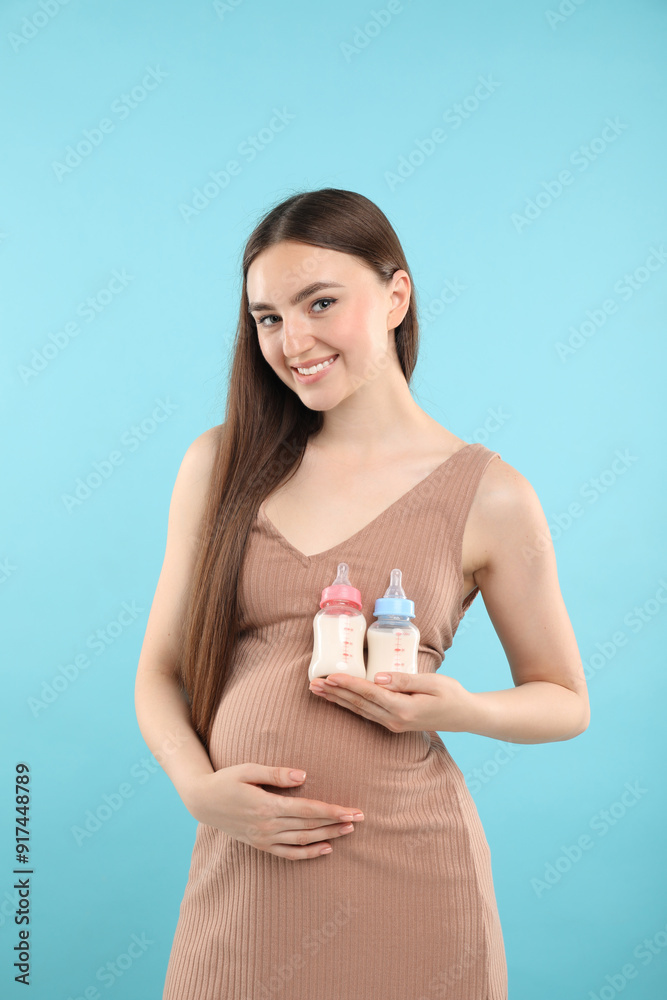Expecting twins. Pregnant woman holding two bottles with milk on light blue background Expecting twins. Pregnant woman holding two bottles with milk on light blue background