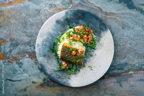 Fried cod fillet with mashed potatoes, fresh prawns and marsh samphire served as top view on a Nordic design plate with text space photo