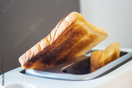 Close-up shot of slightly burnt white bread toasts sticking out of a toaster.