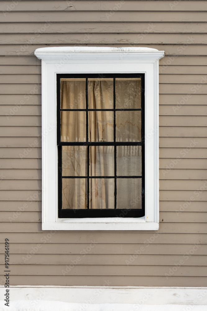 The exterior wall of a beige coloured building is made of narrow horizontal wooden clapboard. There's a single hung closed block glass window with white crown trim molding and black glass dividers. The exterior wall of a beige coloured building is made of narrow horizontal wooden clapboard. There's a single hung closed block glass window with white crown trim molding and black glass dividers.