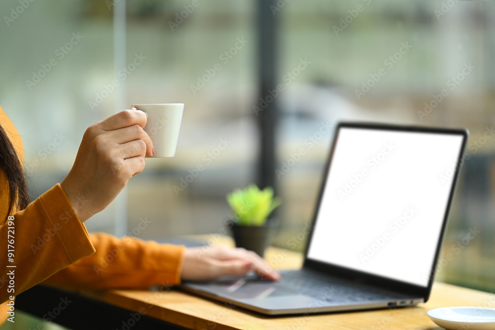 Young woman holding a cup of coffee using laptop on table near glass wall in coffee shop Young woman holding a cup of coffee using laptop on table near glass wall in coffee shop