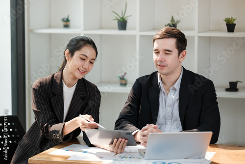 Two people are sitting at a table with laptops and a tablet