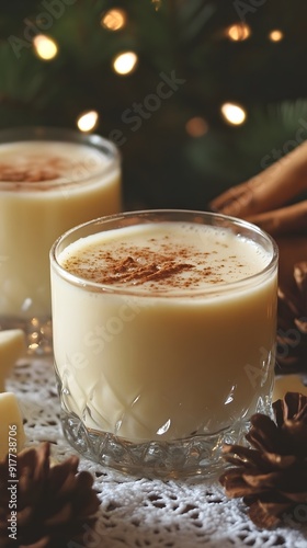 Christmas spiced eggnog white milk drink with cinnamon and anise in a glass mason jar on a light wooden table, white background, Christmas decorations and pine branches around the glasses