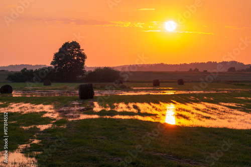 Obraz na płótnie Beautiful rural landscape at sunset moments after a storm. Flooded meadows with hay bales. The setting sun reflecting in puddles w salonie