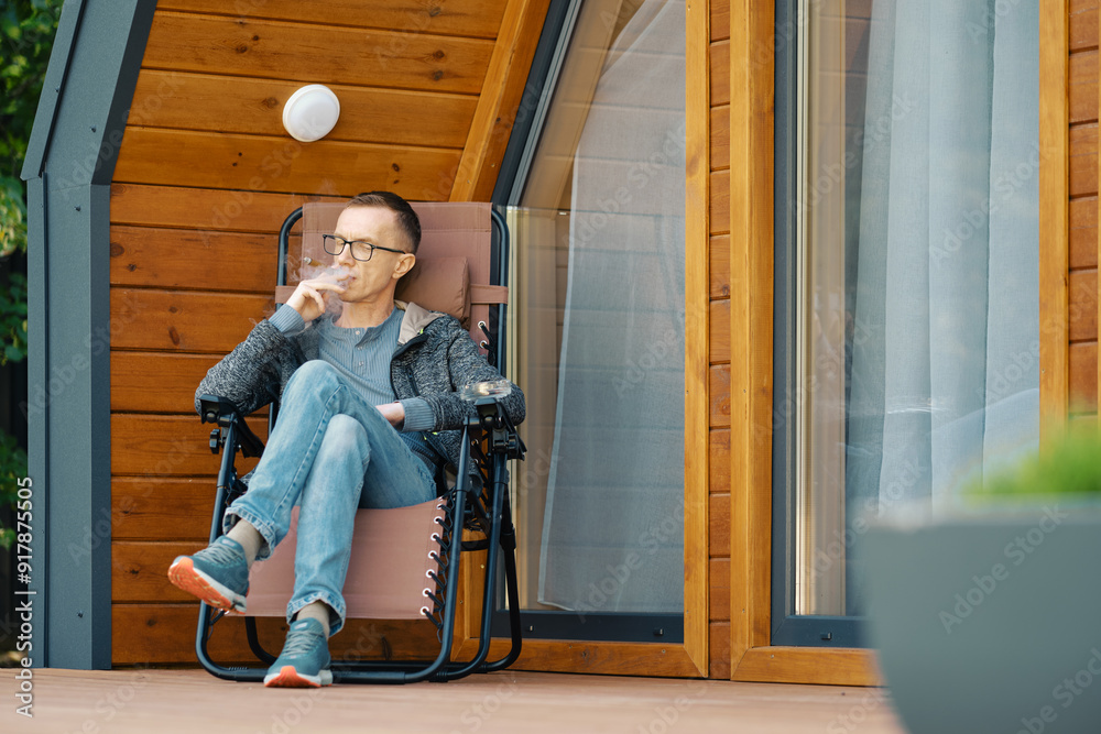 Middle-aged man smoking a cigar while sitting on the terrace of a country house Middle-aged man smoking a cigar while sitting on the terrace of a country house