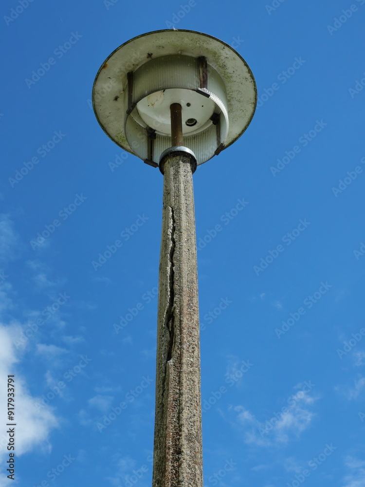 Photo of an old deteriorated street lamp from DDR times. The damaged concrete pole and worn-out light fixture highlight the need for modernization. Photo of an old deteriorated street lamp from DDR times. The damaged concrete pole and worn-out light fixture highlight the need for modernization.