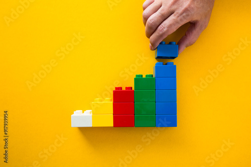 Businessman building a successful growing chart with colourful toy bricks on yellow background