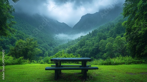 A wooden picnic table sits in a lush green field, overlooking a mountain range