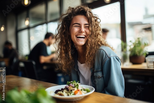 A woman with curly hair is smiling and eating a salad