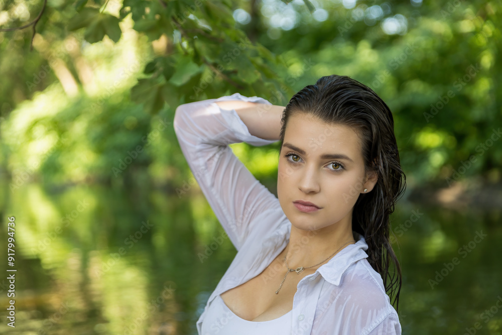 Portrait of beautiful young girl posing with wet hair in the river. The girl touches her hair with one hand. Horizontally. Portrait of beautiful young girl posing with wet hair in the river. The girl touches her hair with one hand. Horizontally.