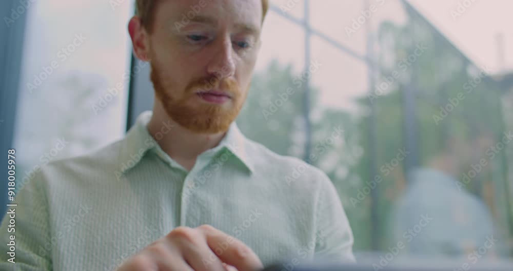 Close facial view of Caucasian man with moustache working on tablet device. Using touchscreen with one finger. Operating with numbers or data on modern technology. Looking at camera and smiling. Close facial view of Caucasian man with moustache working on tablet device. Using touchscreen with one finger. Operating with numbers or data on modern technology. Looking at camera and smiling.
