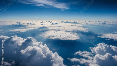 Aerial view of fluffy white clouds bathed in sunlight with a deep blue sky extending to the horizon.