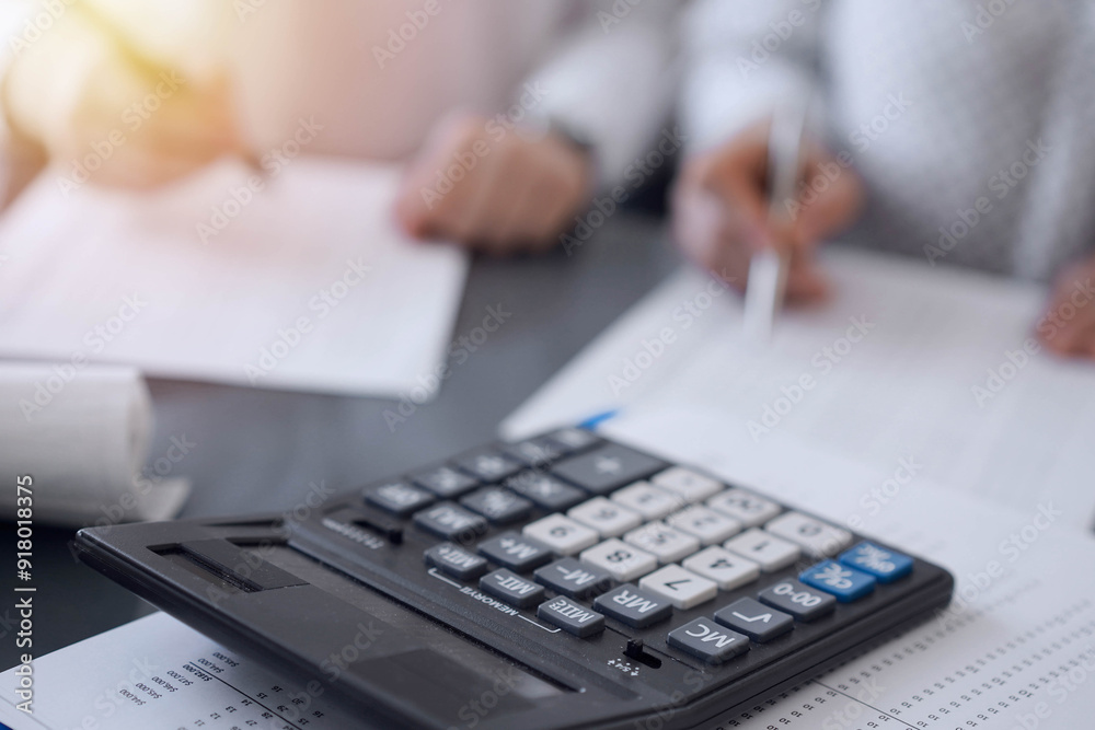 Calculator is waiting to be used while Two accountants are ready to count taxes or make a revenue balance in the background. Business, audit, and taxes concepts