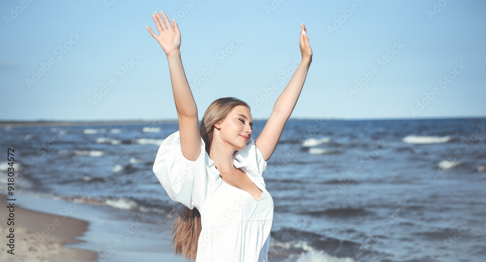 Happy smiling beautiful woman on the ocean beach standing in a white summer dress, raising hands Happy smiling beautiful woman on the ocean beach standing in a white summer dress, raising hands