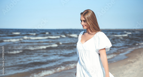 Happy, beautiful woman on the ocean beach standing in a white summer dress, open arms