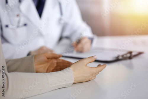 Unknown male doctor and patient woman discussing something while sittingin a darkened clinic, glare of light on the background. Close-up of hands