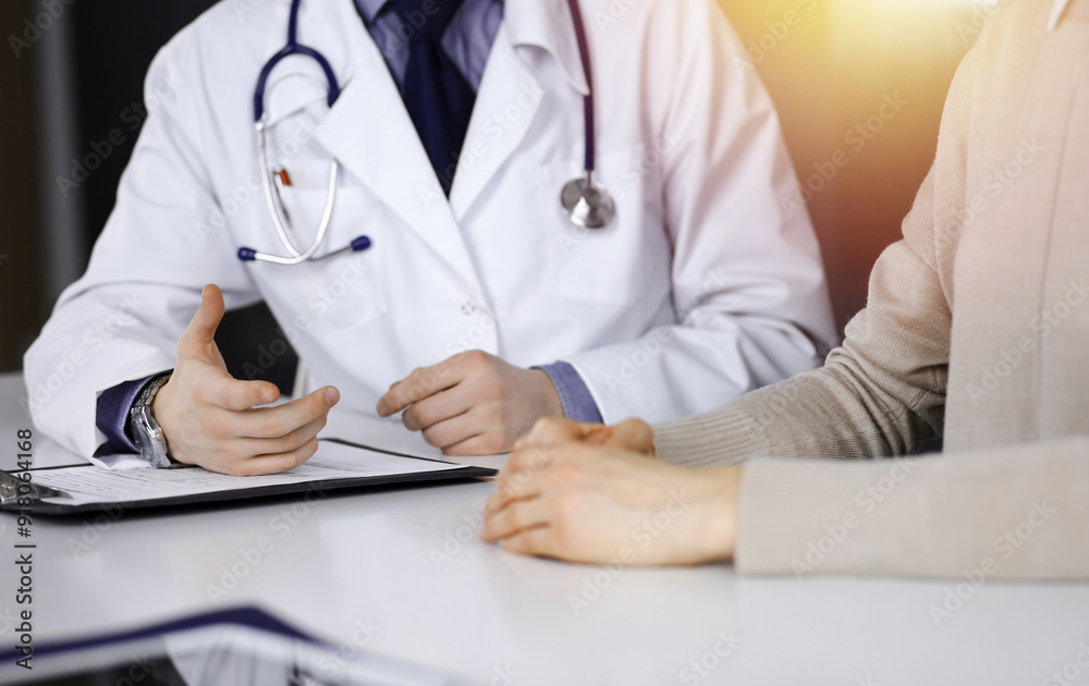 Unknown male doctor and patient woman discussing something while sittingin a darkened clinic, glare of light on the background. Close-up of hands Unknown male doctor and patient woman discussing something while sittingin a darkened clinic, glare of light on the background. Close-up of hands