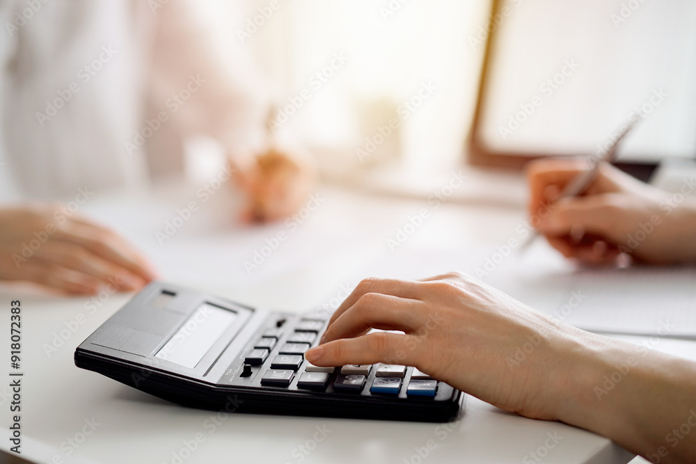 Two accountants using a calculator and laptop computer for counting taxes at white desk in office. Teamwork in business audit and finance Two accountants using a calculator and laptop computer for counting taxes at white desk in office. Teamwork in business audit and finance